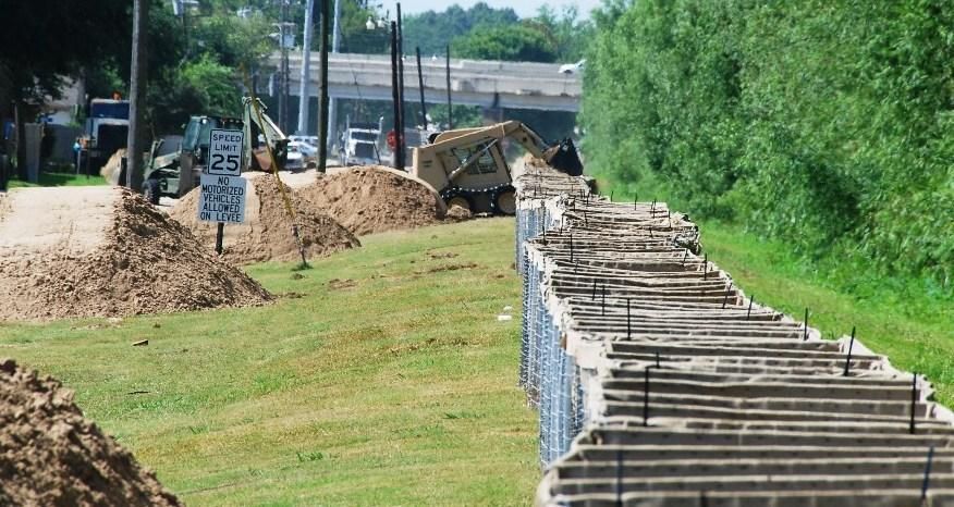 Línea de barreras modulares HESCO a lo largo de un dique, rellenándose con maquinaria durante una defensa contra inundación